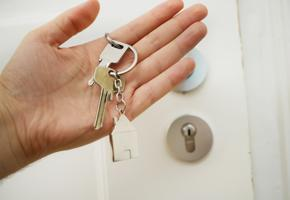 A hand holding a keyring with two keys and a house-shaped charm. 