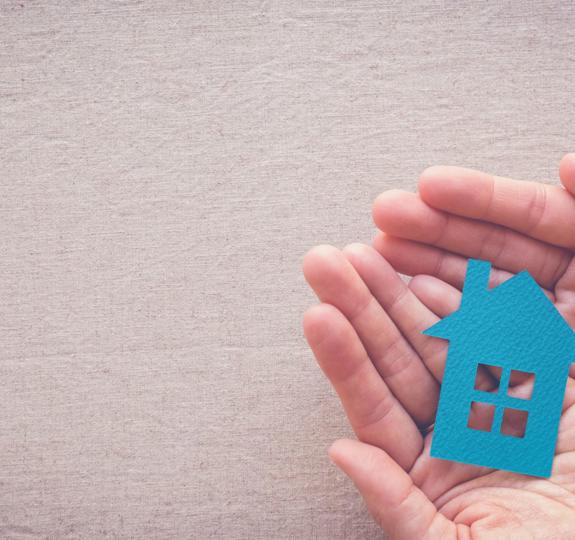 A small blue cut-out shape of a house being held in someone's open hands