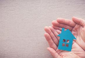 A small blue cut-out shape of a house being held in someone's open hands