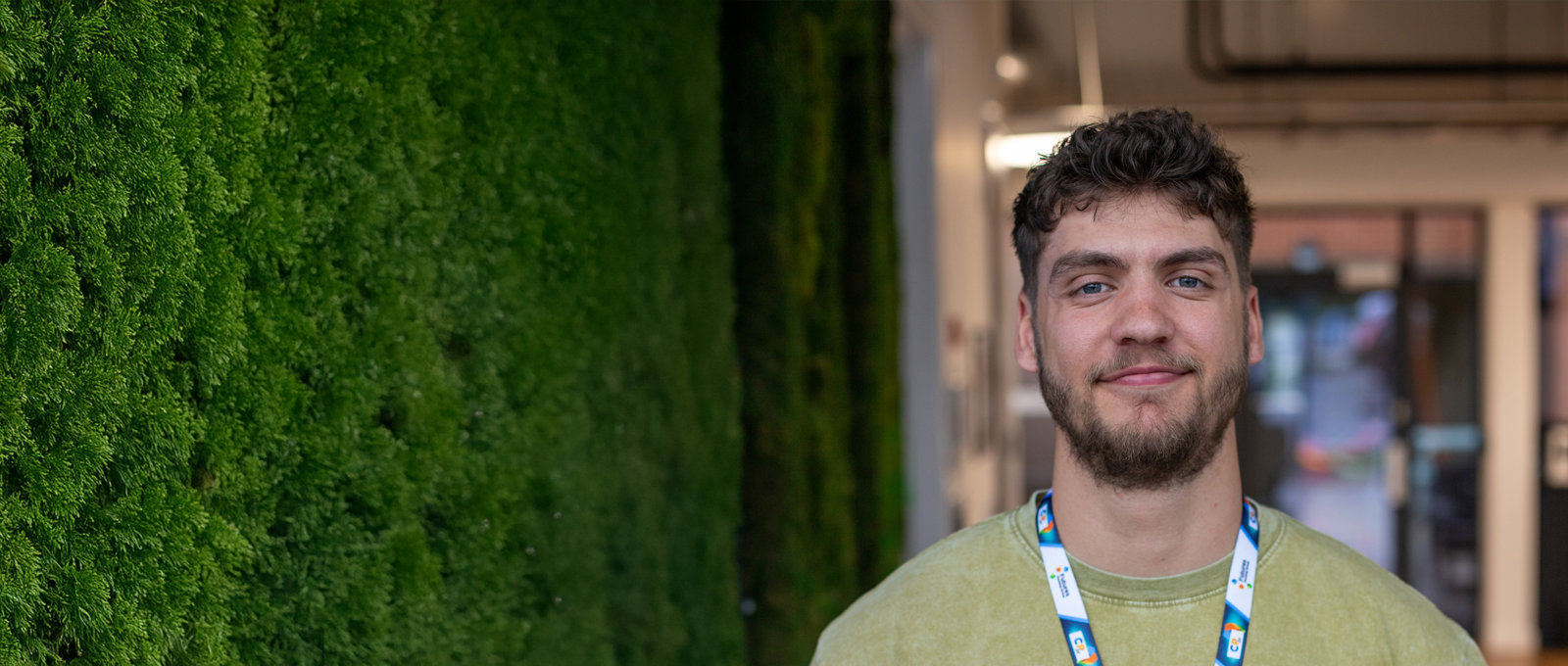 Close-up photo of a man smiling stood next to a green wall