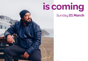 A man in a hat and blue coat sat on a beach. Text reads 'The census is coming Sunday 21 March'. 