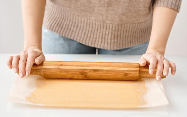 A person in a beige jumper and jeans rolling out pastry.