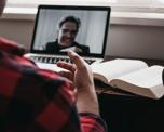 A person sitting at a desk having a video call with a man in glasses on a laptop.