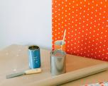 Tins of wallpaper paste and rolls of wallpaper in bright orange patterns.