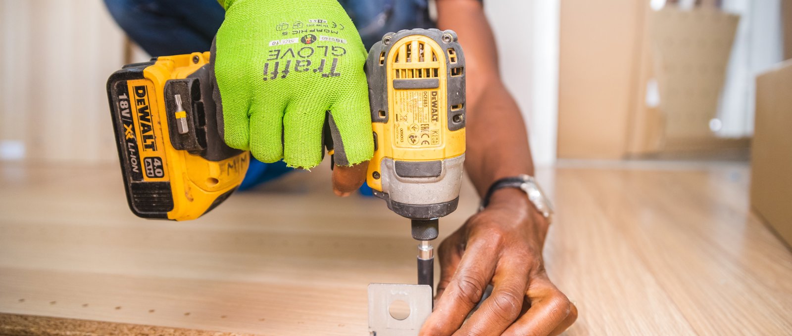 A close up on a person's hands using an electric screwdriver, attaching a metal bracket to a piece of wood.