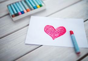 A red heart drawn in crayon on a white piece of paper