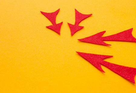 Photo of four red arrows made of felt arranged in a circle, all pointing inwards, on a yellow surface