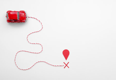 Ariel view of model red toy car connected to a red map point by a winding piece of red and white twisted string