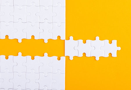 Photo of white jigsaw pieces on an orange surface. Several pieces have been removed from the puzzle in a strip and placed to the side of the jigsaw to create a 'mirror image' effect