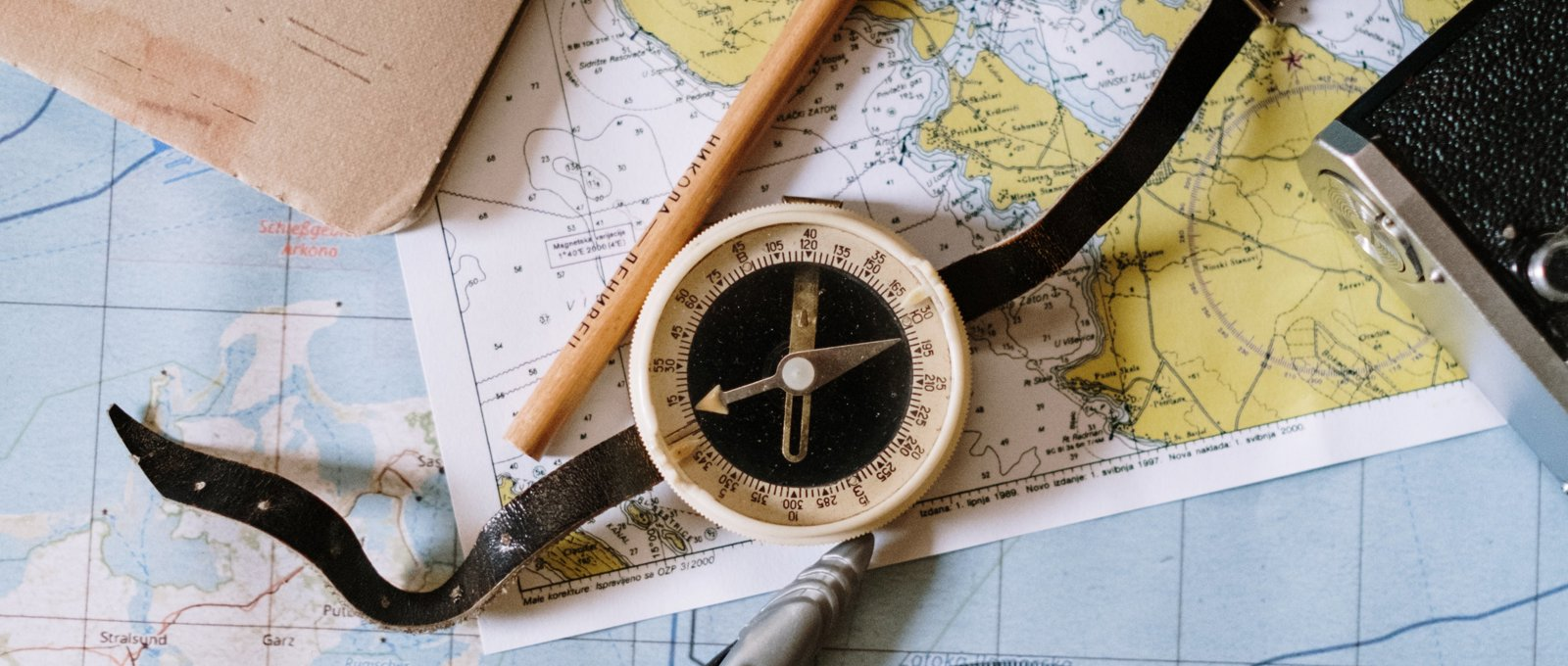 A compass and pencil lying on top of various maps