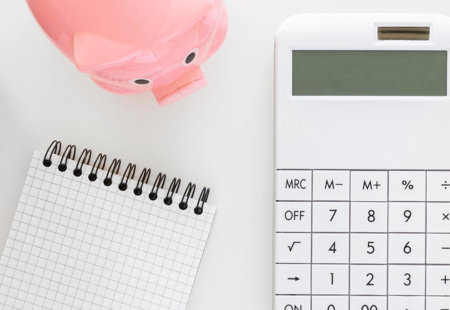 desktop with budgeting tools including calculator, piggy bank, pen, note pad, clock and diary