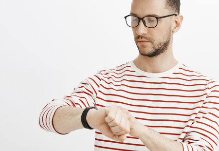 Photo of a young man in a red and white striped top looking impatiently at his watch