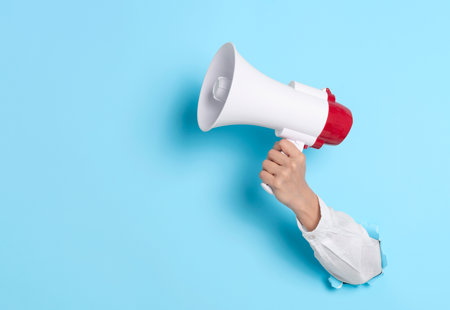 photo of a hand pushed through the light blue background and holding a white and red megaphone