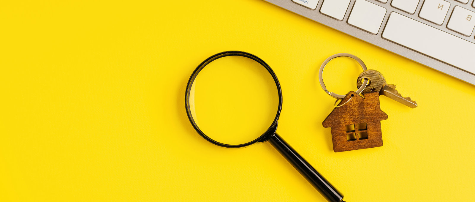 photo of a magnifying glass, a set of house keys, and a keyboard on a bright yellow surface