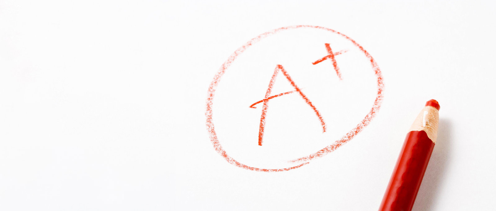 Photo of 'A+' written in red pencil on white paper with the pencil lying next to the writing